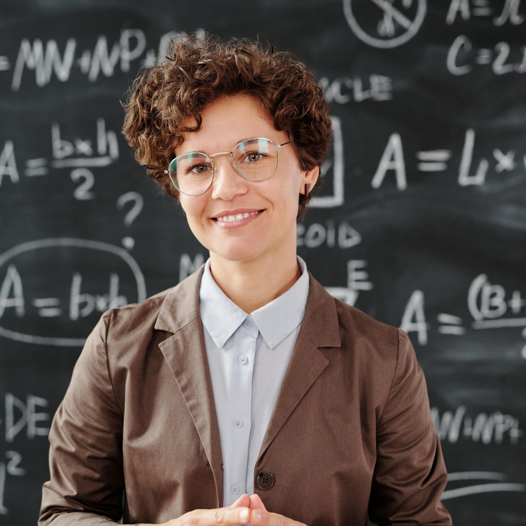 Teacher standing by a blackboard with algebra equations, smiling confidently.